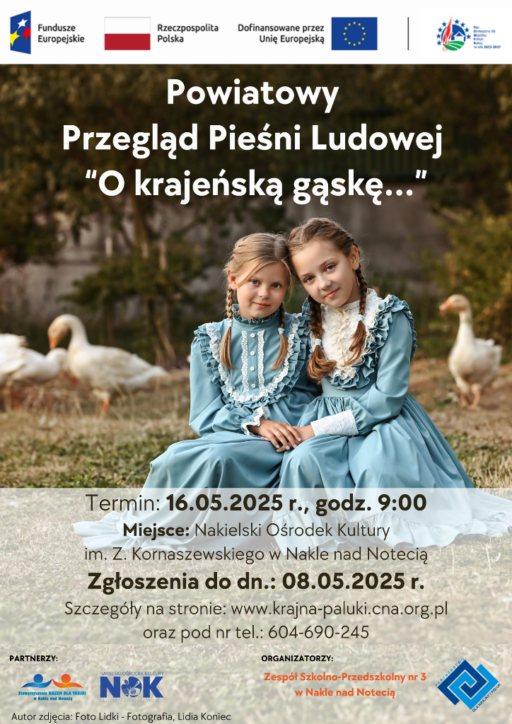 Dwie dziewczynki w niebieskich sukienkach siedzą na trawie a w tle widać gąski.